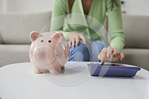 Woman calculate expenses from piggybank on machine