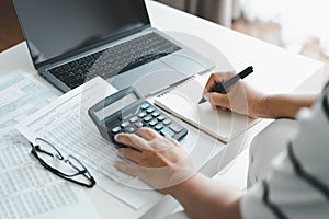 Woman is calculating annual tax, monthly expenses with calculator and filling form of Individual Income Tax Return. Season to pay