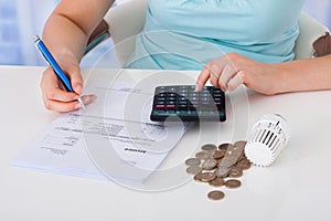 Woman calculating invoice by coins and thermostat at desk photo