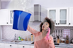 Woman Calling Plumber While Collecting Water From Ceiling