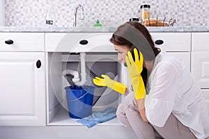 Woman Calling Plumber In Front Of Water Leaking From Pipe