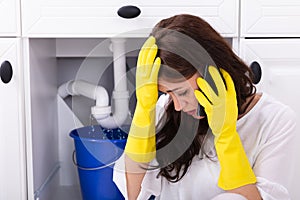 Woman Calling Plumber In Front Of Water Leaking From Pipe