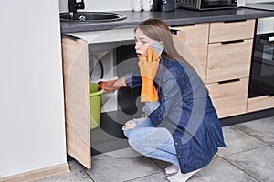 Woman calling plumber while sitting in front of water leaking