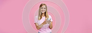 Woman calling taxy via smartphone asking friend address smiling cheerfully at camera holding phone with both hands over photo