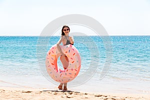 Woman calls to swim in the sea and waves her hand. Girl relaxing with donut on the beach and playing with inflatable ring. Summer