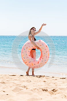 Woman calls to swim in the sea and waves her hand. Girl relaxing on inflatable ring at the beach. Summer holidays and vacation