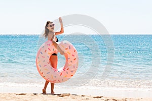 Woman calls to swim in the sea and waves her hand. Girl relaxing on inflatable ring at the beach. Summer holidays and vacation