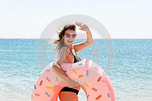 Woman calls to swim in the sea and waves her hand. Girl relaxing on inflatable ring at the beach. Summer holidays and vacation