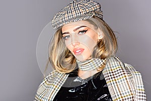 Woman on calm face with make up with checkered accessories. Girl with long hair wears plaid kepi, scarf, grey background