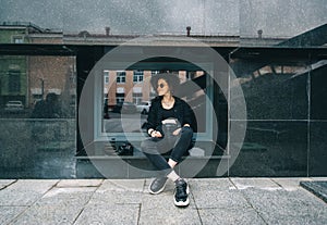 Woman with a camera in the city sitting near the window of a marble building. Woman photographer in black sunglasses