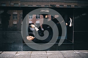 Woman with a camera poses, lying on the back, in the window of a marble building on city street