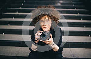 Woman with a camera sitting on stair inside the building. Woman photographer