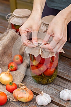 Woman cans pickled tomatoes in glass jars on an old wooden table. Summer harvest.