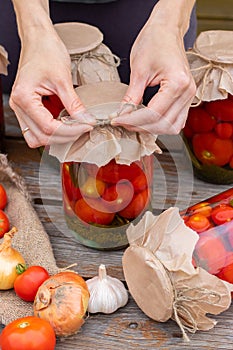 Woman cans pickled tomatoes in glass jars on an old wooden table. Summer harvest.