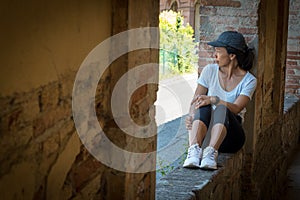 Woman in cap and sneakers sitting in window of portico