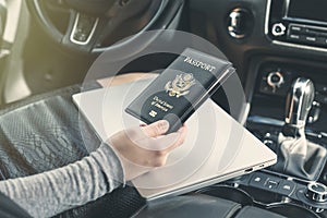 Woman in the car with laptop and american passport. Travel concept.