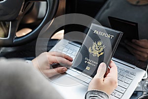 Woman in the car with laptop and american passport. Travel concept.