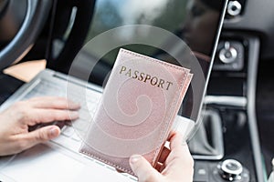 Woman in the car with laptop and passport in a pink cover. Travel concept.