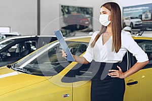 Woman car seller standing near new car wearing protective face mask