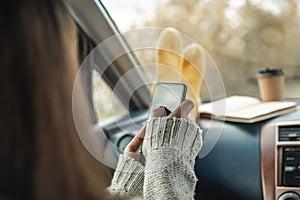 Woman in a car in warm socks is holding a mobile phone gadget. Cozy autumn weekend trip. Freedom of travel