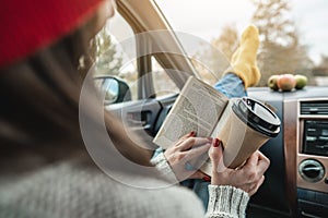 Woman in a car in warm woolen socks yellow is reading a book at sunset. Cozy autumn weekend trip. Freedom of travel