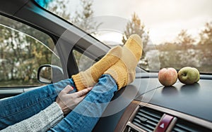 Woman in a car in warm woolen yellow socks on the car dashboard. Cozy autumn weekend trip. Concept of freedom of travel