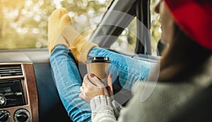 Woman in a car in warm yellow socks is holding a Cup of coffee in hands. Cozy autumn weekend trip. Freedom of travel