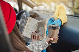 Woman in a car in warm yellow socks is reading a book while sitting in the passenger seat. Cozy autumn weekend trip