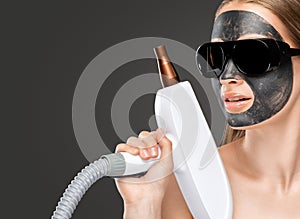 A woman with a carbon mask on her face, a beautician does laser carbon peeling on the problem areas of the skin of a young