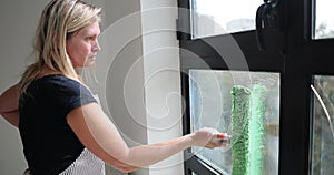 Woman carefully cleans glass door window with scraper and soap