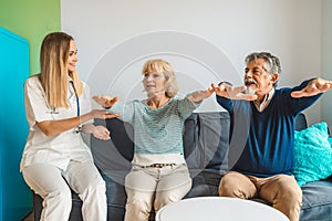 Woman caregiver assisting senior couple at nursing home, showing them some exercises