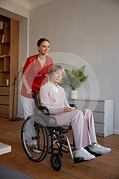 Woman caregiver preparing elderly lady in wheelchair for walk