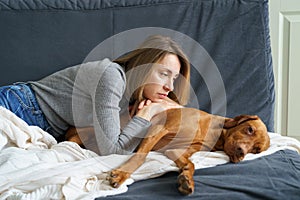 Woman caring of old sick dog. Unhappy female lying on couch embracing tired ill vizsla after illness