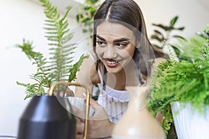 Woman caring for plants next to steam aroma oil diffuser on the table at home, steam from humidifier. Humidification of air in