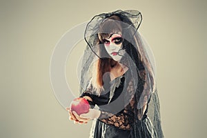 Woman in a carnival costume of a witch or a dead bride holding an apple in her hands, gothic woman in witch costume on gray