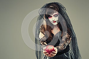 Woman in a carnival costume of a witch or a dead bride holding an apple in her hands, gothic woman in witch costume on gray
