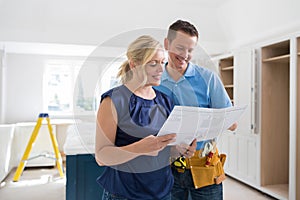 Woman With Carpenter Looking At Plans For New Kitchen