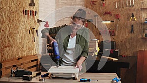 Woman carpenter with safety goggles working with drill in workshop