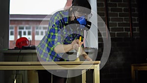 Woman carpenter smacks wood dust from table top with brush in workshop.