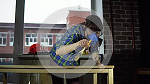 Woman carpenter smacks wood dust from table top with brush in workshop.