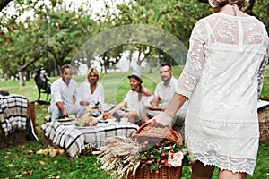 Woman carries basket with dry plants. Group of adult friends have a rest and conversation in the backyard of restaurant
