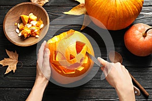 Woman carving Halloween pumpkin head jack lantern on wooden table