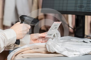 Woman cashier, seller scanning and reading  barcode from clothes using barcode scanner in female clothing store.