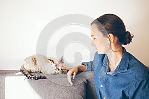 Woman in casual clothes is cuddling her cat. Cat is purring, feeling happy and relaxed. Woman is touching and playing with cute