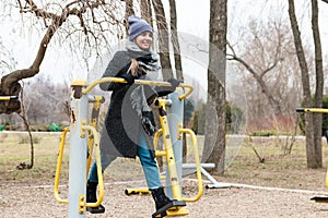 Woman in casual clothes exercising on outdoor gym in park in spring