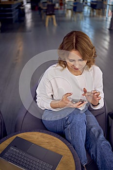 a woman in casual clothes sits on a bean bag and searches using the phone