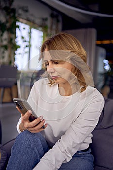 a woman in casual clothes sits on a bean bag and searches using the phone