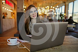 Woman in casual clothes working on a laptop sitting in a cafe. Smiling sitting with a cup of coffee on the table