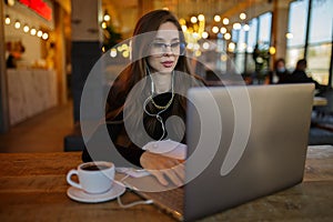Woman in casual clothes working on a laptop sitting in a cafe. Smiling sitting with a cup of coffee on the table