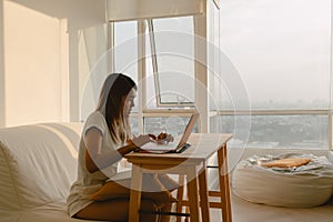 Woman in casual clothes working and typing with her computer laptop in her apartment in concept of work from home